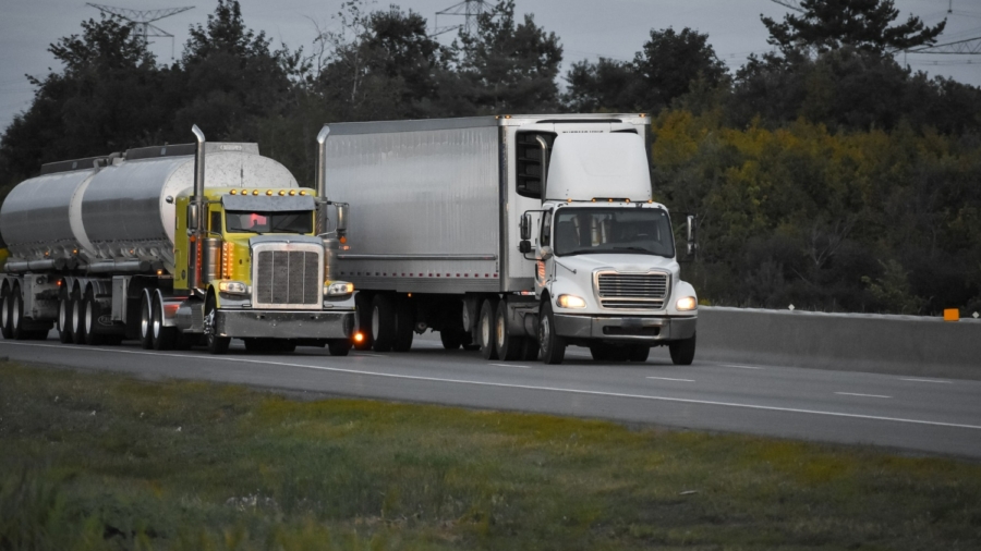 Two large semi-trucks drive side by side on a highway near trees and greenery, capturing the essence of Road Freight in the UAE under overcast skies with power lines visible in the background.